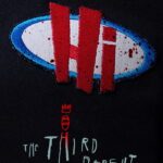 Affiche teaser de The Third Parent : un badge « Hi » ensanglanté sur un tissu sombre, avec le titre manuscrit en bas